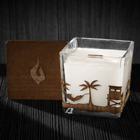 Image of a 3x3x3 soy candle featuring a mahogany scent, crackling wood wick, with a wood lid and an Beach scene wrap design.