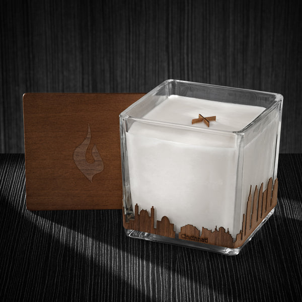 Image of a 4x4x4 soy candle featuring a mahogany scent, crackling wood wick, with a wood lid and an Cincinnati skyline wrap design.