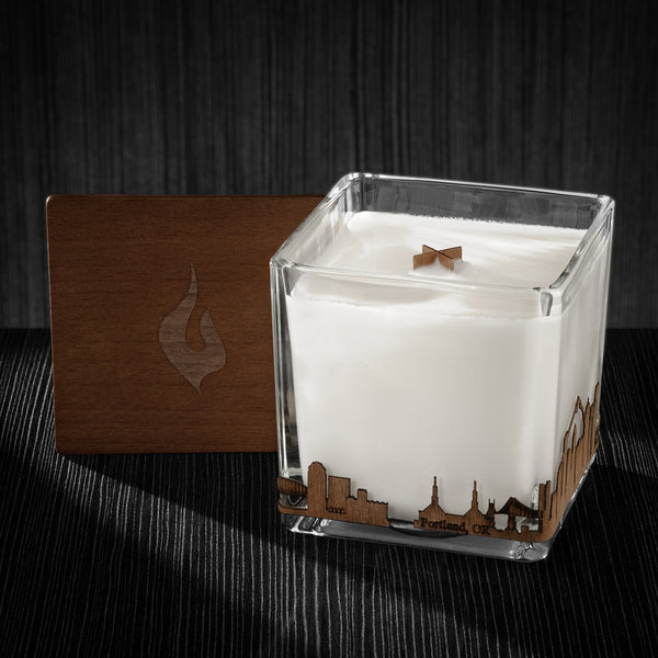 Image of a 4x4x4 soy candle featuring a mahogany scent, crackling wood wick, with a wood lid and a Portland skyline wrap design.