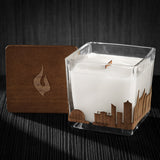 Image of a 3x3x3 soy candle featuring a mahogany scent, crackling wood wick, with a wood lid and a Raleigh City skyline wrap design.
