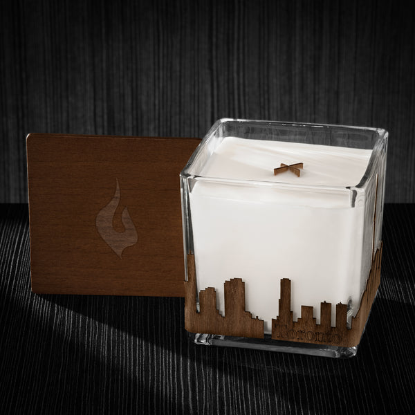 Image of a 4x4x4 soy candle featuring a mahogany scent, crackling wood wick, with a wood lid and a Toronto skyline wrap design.